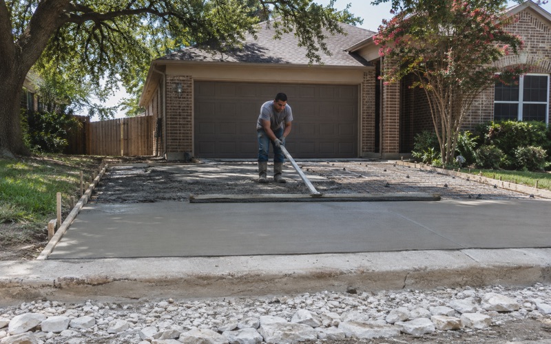 A screed board being drawn across a freshly placed concrete driveway in San Marcos, struck off flat behind and heaped wet ahead.