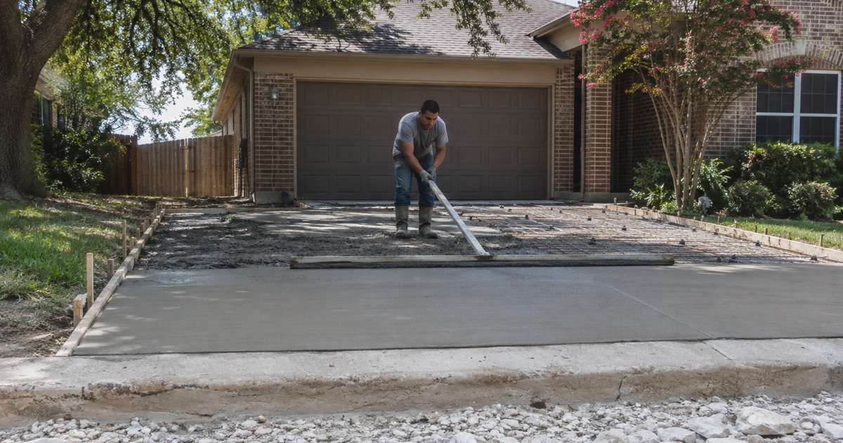 A screed board being drawn across a freshly placed concrete driveway in San Marcos, struck off flat behind and heaped wet ahead.